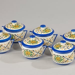 Könnte beinhalten: Satz mit sechs kleinen Keramikschalen mit Deckeln. Die Schalen sind weiß mit blauen und gelben Blumendesigns. Die Deckel haben ein gewebtes Muster.