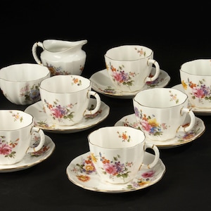 May include: A vintage tea set featuring white porcelain cups, saucers, a sugar bowl, and a creamer. Each piece is adorned with a floral pattern in shades of pink, purple, yellow, and green, with gold trim. The set includes six cups and saucers.