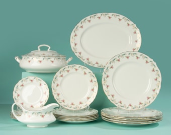 May include: A set of white porcelain dinnerware with a floral pattern in shades of pink and green. The set includes a large oval platter, a round serving bowl, a gravy boat, and several plates of varying sizes.