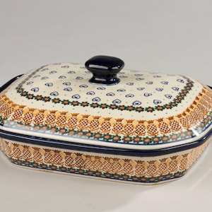 May include: Rectangular ceramic casserole dish with a lid. The dish has a cream background with blue hearts and floral patterns. The rim and lid handle are dark blue, and the dish has a decorative border.
