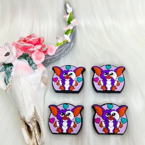 May include: Four purple, orange, and white cartoon character charms with hearts. The characters are on a white fuzzy background.