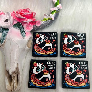 May include: Four black square-shaped stickers with a cartoon panda bear holding a donut. Each sticker has the text "Cute -and- Lazy" in white letters. The panda bears are wearing a red and white striped donut.