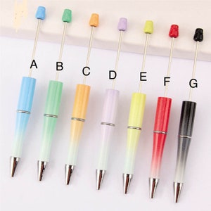 May include: Set of 8 gradient color ballpoint pens with different colored tops. The pens are arranged in a row from left to right: light blue, light green, orange, light purple, yellow, red, gray, and black.