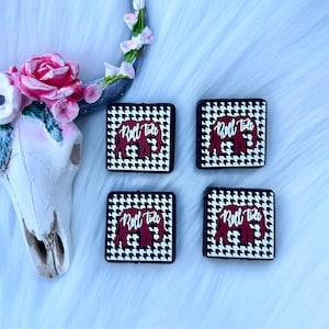 May include: Four square coasters with a black and white houndstooth pattern. Each coaster features a red elephant with the words "Roll Tide" printed on it.