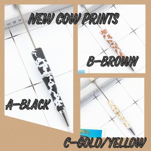 May include: Three pens with cow print designs. The pens are black, brown, and gold with white spots. The text on the image reads "NEW COW PRINTS", "A-BLACK", "B-BROWN", and "C-GOLD/YELLOW".