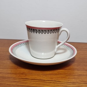 Może przedstawiać: Biały ceramiczny kubek do kawy i spodek z różowym i czarnym geometrycznym wzorem wokół krawędzi.