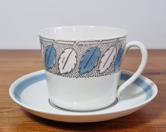 Puede incluir: Una taza de té y un platillo de cerámica blanca con un patrón de hojas azules y rosas. La taza tiene un asa y el platillo tiene una banda azul alrededor del borde.