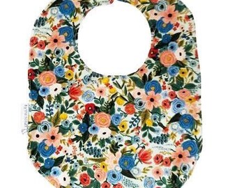 May include: A floral baby bib with a white background. The bib is covered in a pattern of red, blue, yellow, and peach flowers with green leaves. The bib has a rounded shape with a circular cutout for the neck and a snap closure.