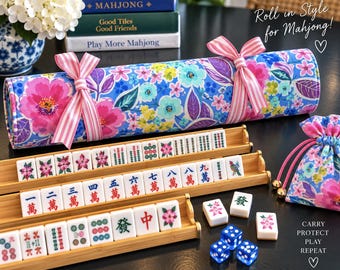 May include: A floral fabric roll tied with pink and white striped ribbons, three bamboo tile racks holding mahjong tiles with Chinese characters and floral designs, a matching drawstring pouch, and two blue dice with white pips.