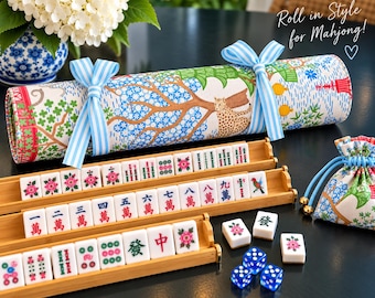 May include: A rolled fabric mahjong mat with a colorful leopard and tree print, tied with light blue striped ribbons. Includes three bamboo tile racks, white mahjong tiles with red, green, and blue markings, three blue dice, and a matching drawstring bag.