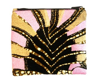 May include: A rectangular, zippered pouch with a vibrant, abstract pattern. The design features a central black, leaf-like shape with white dotted lines, framed by gold and pink geometric elements. The zipper is black.