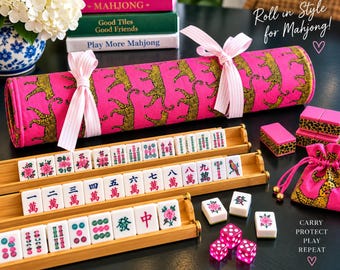 May include: A Mahjong set featuring white tiles with colorful symbols and characters, arranged on three bamboo racks. Includes a bright pink fabric roll with a leopard print pattern, tied with light pink striped ribbons, and a matching drawstring bag.