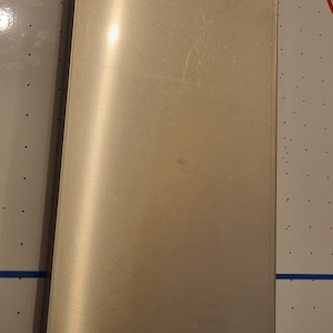 Op de afbeelding: Een zilveren metalen plaat met drie kleine gaten. De plaat is glad en heeft een lichte glans.