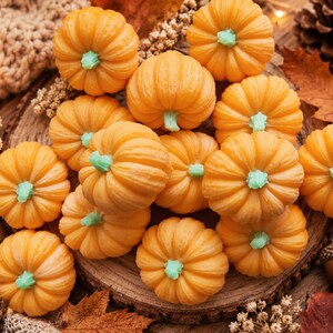 May include: A collection of small, orange pumpkin-shaped items with light green stems. Each pumpkin features a ribbed texture and a rounded form. The items are arranged in a cluster, showcasing their vibrant orange colour and distinct green stems, creating a uniform appearance across the group of decorative objects.