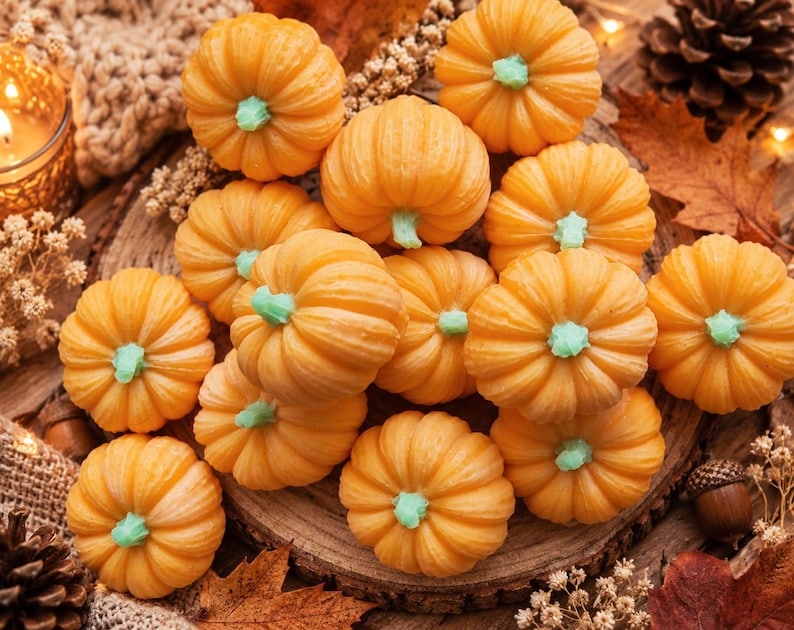 May include: A collection of small, orange pumpkin-shaped items with light green stems. Each pumpkin features a ribbed texture and a rounded form. The items are arranged in a cluster, showcasing their vibrant orange colour and distinct green stems, creating a uniform appearance across the group of decorative objects.