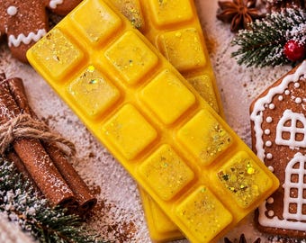 Puede incluir: Dos barras rectangulares de cera aromática de color amarillo con una cuadrícula de diez segmentos individuales. La cera tiene un acabado liso con partículas de purpurina dorada incrustadas en la superficie, creando un aspecto brillante y texturizado.