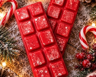 Puede incluir: Dos barras rectangulares de cera aromática roja, cada una con diez segmentos individuales. La cera tiene una superficie texturizada con partículas de purpurina plateada incrustadas. Las barras están dispuestas en orientación vertical.