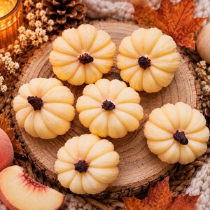 May include: Six small, pale yellow, pumpkin-shaped wax candles with dark brown stems, arranged on a circular wooden slice. The candles feature a ribbed, rounded surface texture and are positioned together on the textured wood grain surface.