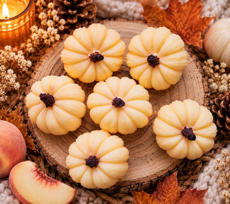 May include: Six small, pale yellow, pumpkin-shaped wax candles with dark brown stems, arranged on a circular wooden slice. The candles feature a ribbed, rounded surface texture and are positioned together on the textured wood grain surface.