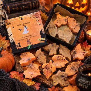 May include: A square box labelled 31st October Soy Wax Melts with a ghost and pumpkin illustration, accompanied by an open black box containing leaf-shaped wax melts in shades of orange and brown, scattered with colourful glitter and dried bits.