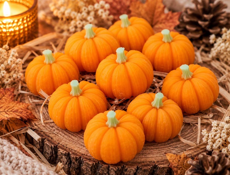 May include: A collection of nine small, vibrant orange pumpkins with light green stems, arranged in a cluster. Each pumpkin features distinct vertical ridges and a smooth, rounded shape, creating a uniform appearance across the group.