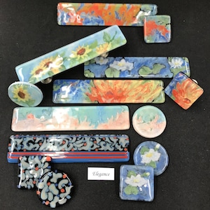 May include: Assortment of colorful glass cabinet knobs with floral and abstract designs. The knobs are in various shapes and sizes, including round, square, and rectangular. The text "Elegance" is visible on a white label.