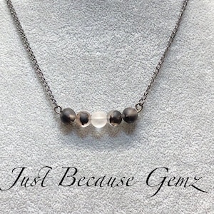 May include: A silver chain necklace with five round beads. The beads are black, white, and gray.