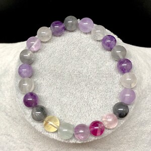 Puede incluir: Una pulsera de cuentas con una variedad de piedras preciosas coloridas. La pulsera incluye cuentas redondas en tonos de morado, gris, rosa, amarillo y transparente. Las cuentas est&aacute;n ensartadas en un cord&oacute;n el&aacute;stico transparente, creando un accesorio vibrante y llamativo.