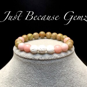 May include: A bracelet made with green, pink, and white beads. The bracelet is on a light gray surface.