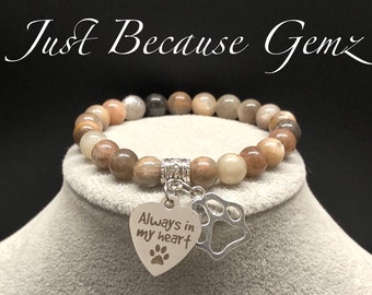 May include: A brown and gray gemstone bracelet with a silver charm that says "Always in my heart" with a paw print.