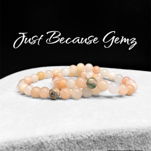 Puede incluir: Dos pulseras hechas de cuentas de color rosa claro y blanco. Una pulsera tiene una cuenta moteada de verde y marrón.