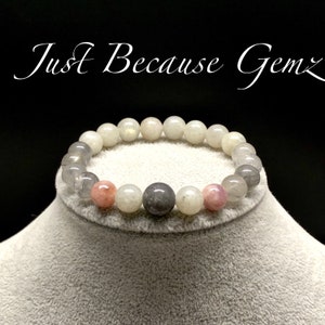 May include: A white, gray, and pink beaded bracelet with a silver charm. The bracelet is made of natural stones and is perfect for everyday wear.