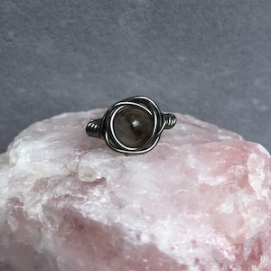 May include: A silver wire wrapped ring with a clear quartz stone in the center.