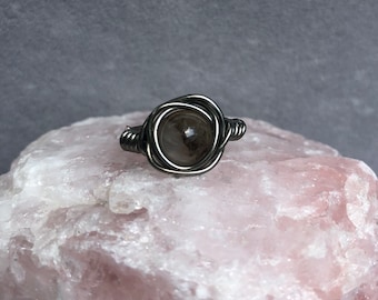 May include: A silver wire wrapped ring with a clear quartz stone in the center.