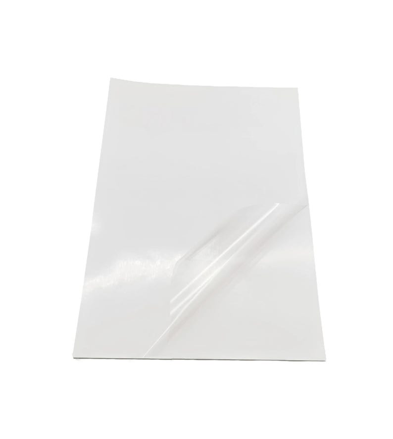 May include: A white sheet of adhesive-backed paper with a clear protective layer partially peeled back.