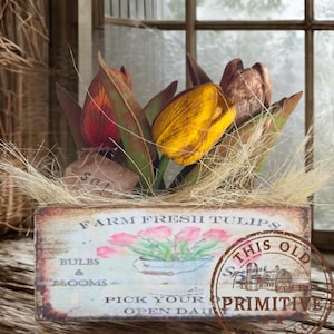 May include: A wooden box with the text "FARM FRESH TULIPS" and a watercolor illustration of pink tulips. The box contains faux tulips in shades of yellow, red, and brown, with green leaves and dried grass.
