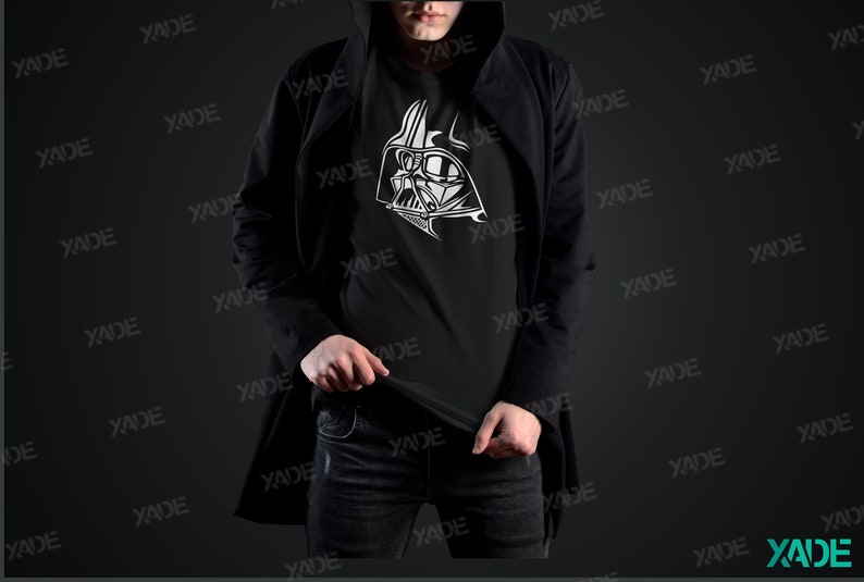 May include: A black t-shirt with a white graphic of Darth Vader's helmet. The person wearing the shirt is wearing a black jacket and blue jeans.
