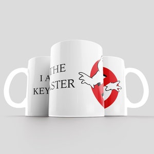 May include: Three white ceramic mugs with black text and a red and white graphic. The text on the mugs reads "I am the Keymaster". The graphic is a red circle with a white ghost inside. The ghost has its arms outstretched and is flying through the air.