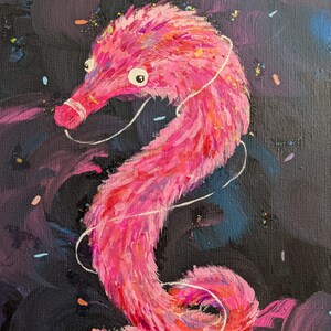 Pode incluir: Uma criatura rosa e peluda com forma de verme com olhos grandes e um nariz rosa, pintada em um fundo escuro com confete colorido.