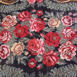 May include: A vintage rug with a floral pattern featuring red, pink, and white roses on a dark blue background. The rug has a detailed design with green leaves and stems.