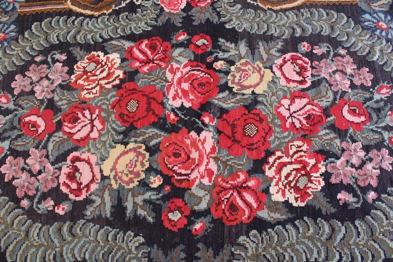 May include: A vintage rug with a floral pattern featuring red, pink, and white roses on a dark blue background. The rug has a detailed design with green leaves and stems.