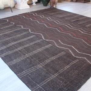 May include: A dark brown woven rug with a geometric pattern. The rug has a striped pattern on one side and a chevron pattern on the other side.