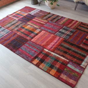 K&ouml;nnte beinhalten: Ein bunter Patchwork-Teppich mit einer Vielzahl von roten, orangefarbenen, blauen und schwarzen Farbt&ouml;nen. Der Teppich ist aus gewebtem Stoff gefertigt und hat einen abgenutzten, Vintage-Look.