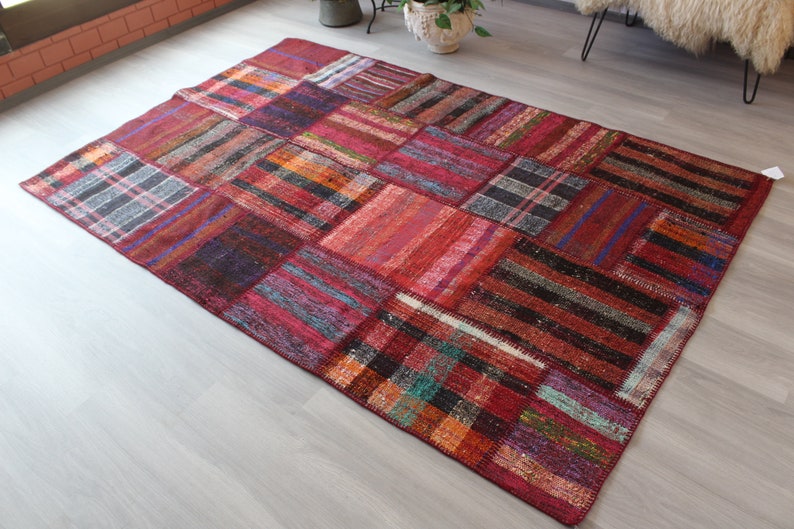 K&ouml;nnte beinhalten: Ein bunter Patchwork-Teppich mit einer Vielzahl von roten, orangefarbenen, blauen und schwarzen Farbt&ouml;nen. Der Teppich ist aus gewebtem Stoff gefertigt und hat einen abgenutzten, Vintage-Look.