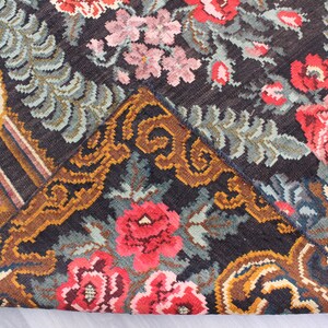 May include: Close-up of a vintage rug with a floral pattern. The rug is made of wool and has a dark background with colorful flowers and leaves. The rug is in good condition and has a unique design.