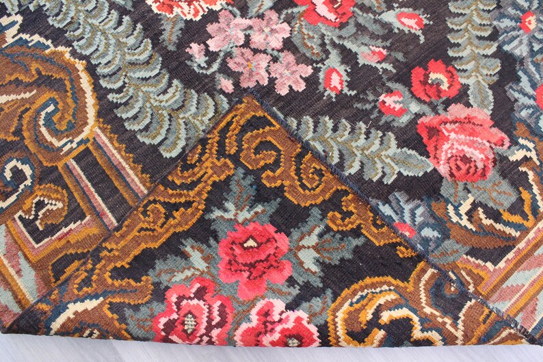 May include: Close-up of a vintage rug with a floral pattern. The rug is made of wool and has a dark background with colorful flowers and leaves. The rug is in good condition and has a unique design.