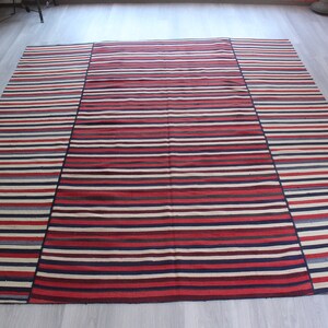 Può includere: Un tappeto a strisce con strisce rosse, bianche e blu. Il tappeto è realizzato in materiale tessuto e ha un bordo con frange.