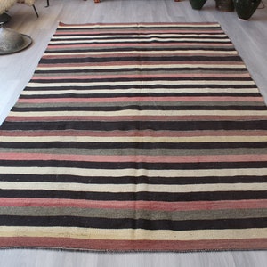 May include: A striped rug with alternating bands of black, white, pink, and gray. The rug has a woven texture and a simple design.