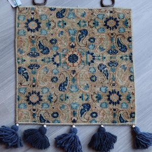 以下が含まれることがあります： 青、茶色、ベージュの paisley 柄の装飾的な壁掛けタペストリー。タペストリーの下部にはフリンジのタッセルが付いています。