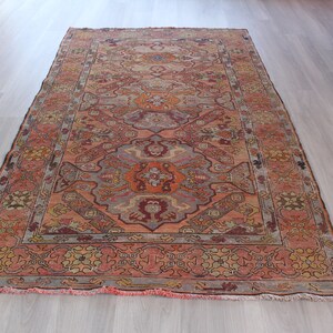 May include: A vintage rug with a faded, intricate design in shades of pink, orange, and blue. The rug has a central medallion and a border with floral motifs.